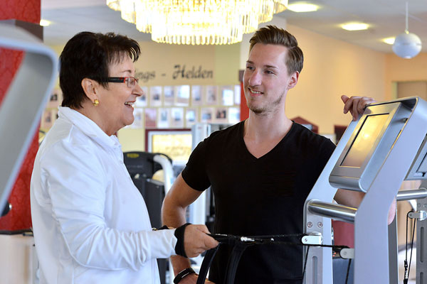 Trainer begleitet Patientin bei Übung an einem digitalen Trainingsgerät
