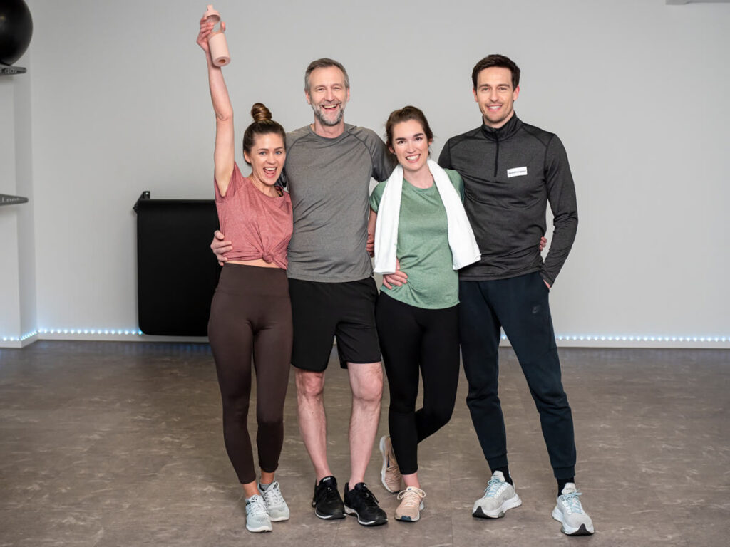 Vier sportlich gekleidete Personen stehen lachend und entspannt nebeneinander nach dem Training